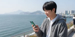 2026 부산 미취업 청년 지원 바닷바람 맞으며 해운대에서 스마트폰으로 청년도전지원사업 신청 확인하는 20대 청년이다